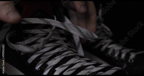 A player in hockey, ties laces on skates, a black background.