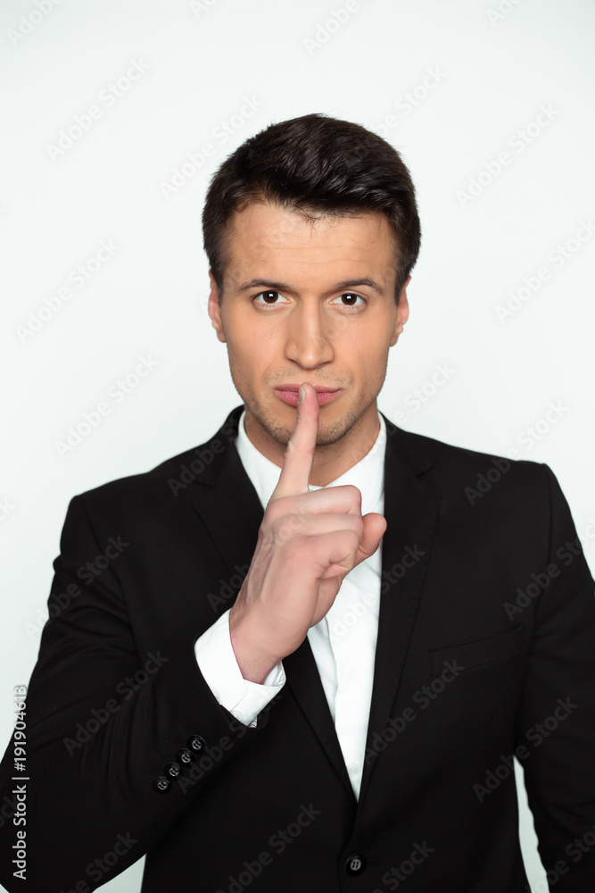 Hush please. A young confident handsome man in a black jacket holds a finger near his lips and looks into the camera. Hush please. A young confident handsome man in a black jacket holds a finger near his lips and looks into the camera.