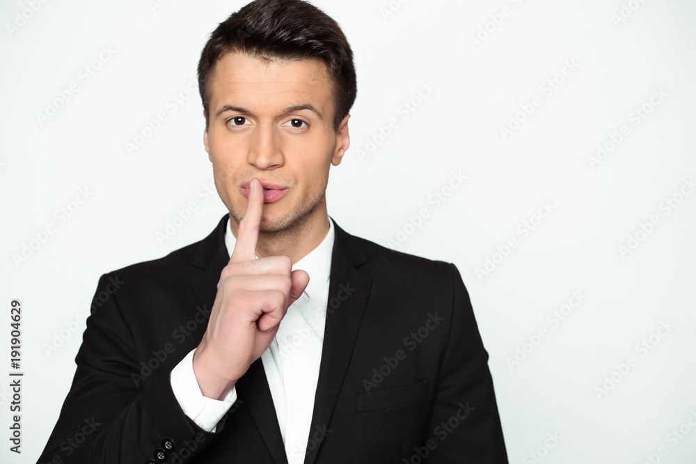 Hush please. A young confident handsome man in a black jacket holds a finger near his lips and looks into the camera. Hush please. A young confident handsome man in a black jacket holds a finger near his lips and looks into the camera.