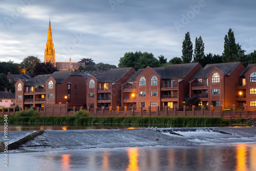 Evening view of the city of Exeter. The river Exe and houses near the shore. A church is seen suspended against a dark blue sky. Devon. UK