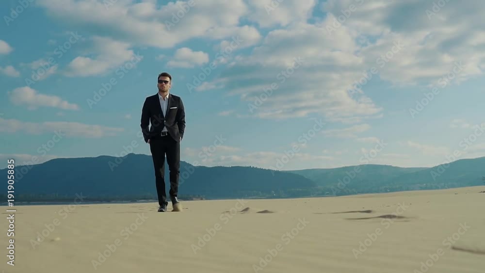 a young stylish man in an expensive jacket and fashionable sunglasses walks through the desert with a serious and important look, faces look around, he looks like a golden youth a young stylish man in an expensive jacket and fashionable sunglasses walks through the desert with a serious and important look, faces look around, he looks like a golden youth