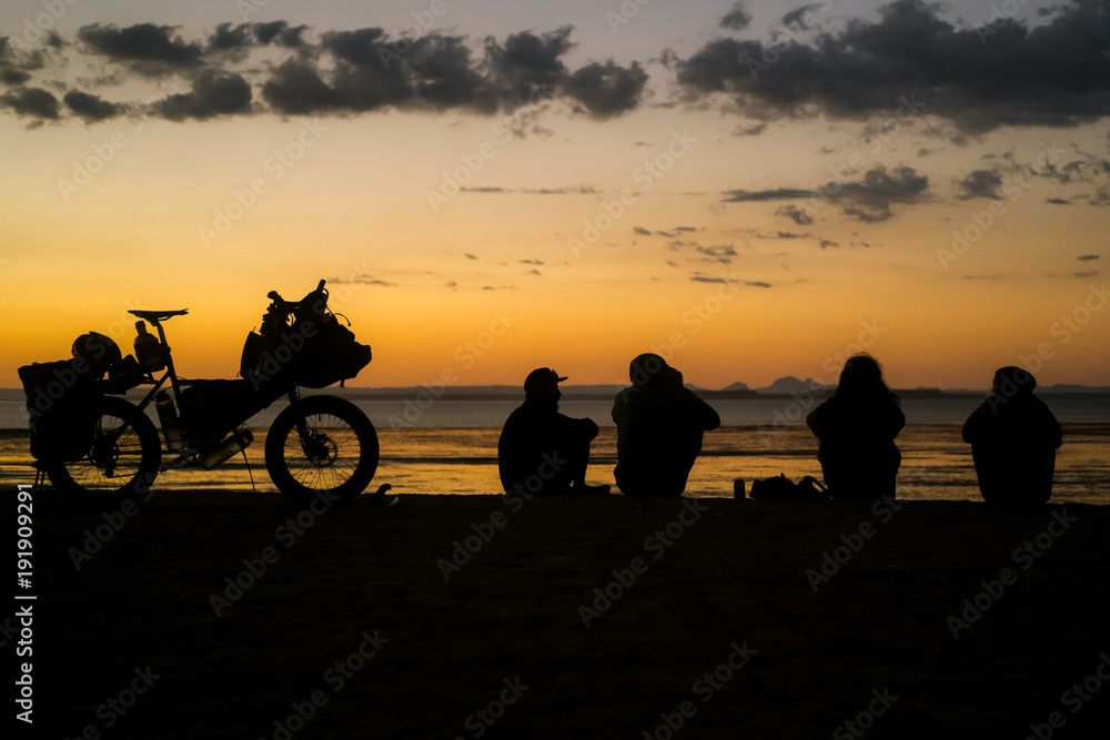 Four people sit on a cliff above the sea in Baja California at sunset next to a loaded touring bicycle with a view of the ocean