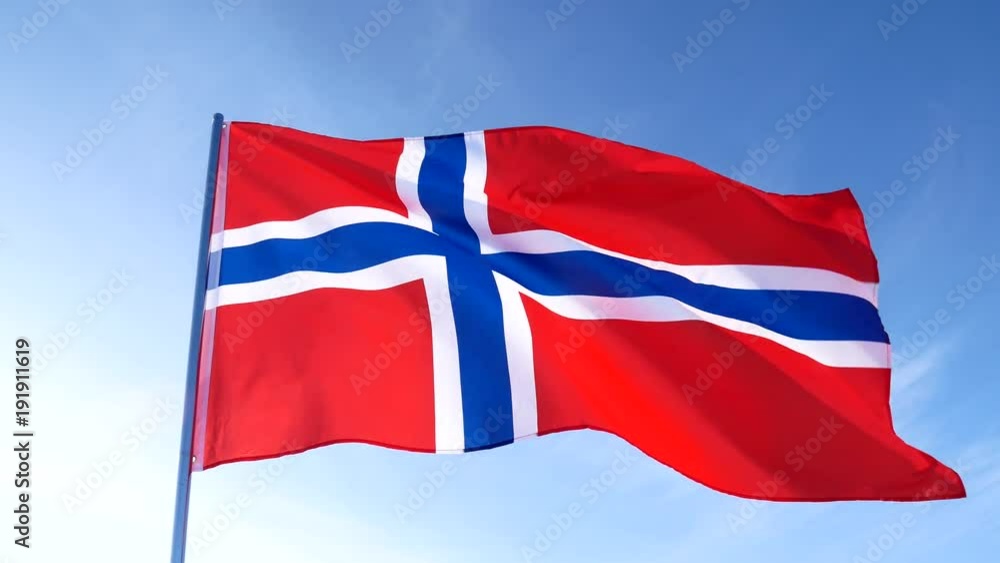 Red with blue cross Norwegian national flag is slowly waving in the blue clear sky on white flagpole Red with blue cross Norwegian national flag is slowly waving in the blue clear sky on white flagpole