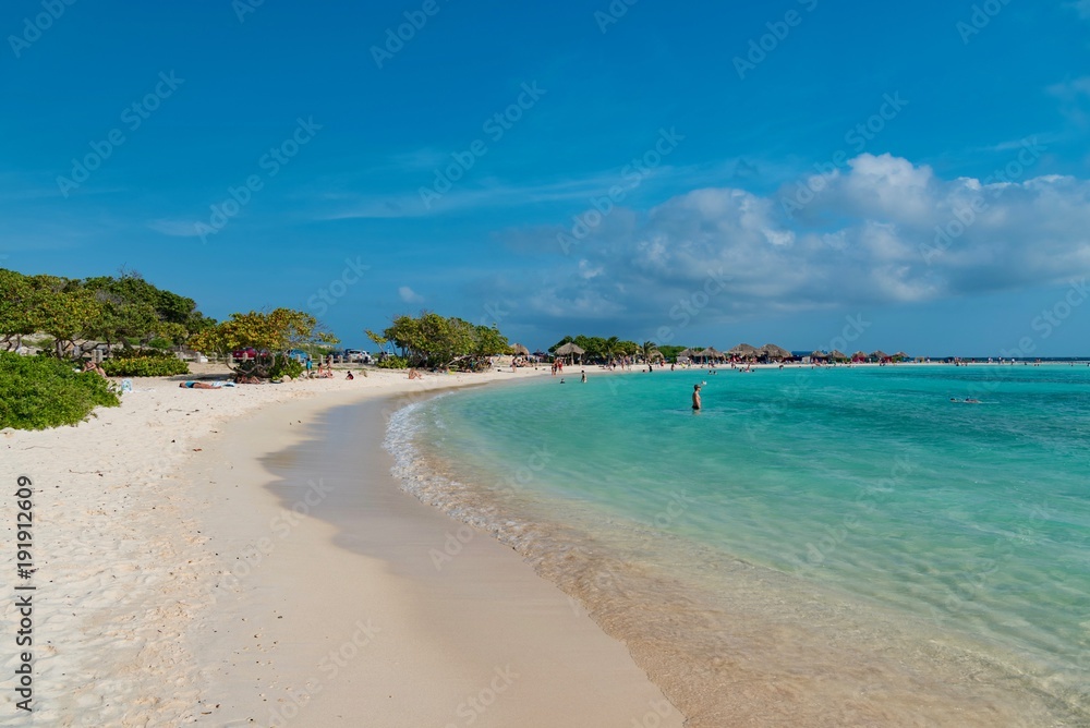 tropical Caribbean beach at sunset with straw umbrellas and white sand island of Aruba