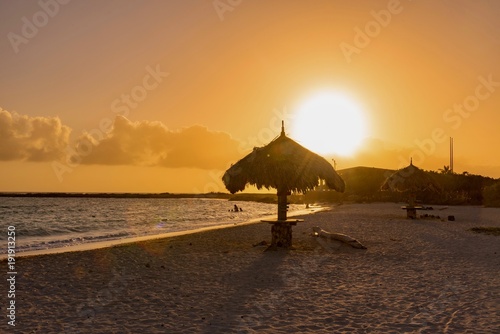 tropical Caribbean beach at sunset with straw umbrellas and white sand island of Aruba