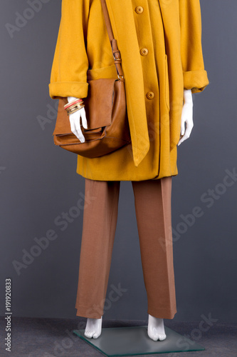 Women stylish handbag and trousers. Female mannequin clothed in elegant topcoat and trousers. Feminine fashion attire and accessories.