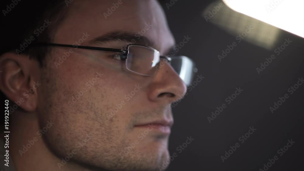 Portrait of young excited unshaved caucasian guy in glasses with light reflections working on computer at night, close up Portrait of young excited unshaved caucasian guy in glasses with light reflections working on computer at night, close up