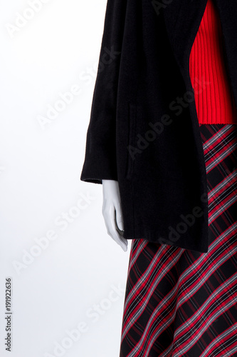 Close up black coat and striped skirt. Female mannequin in red sweater and black overcoat close up, copy space. Boutique of ladies outfit.