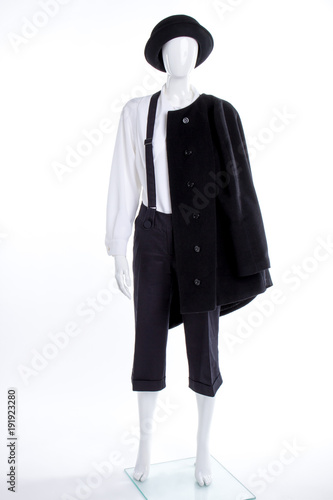 Black hat and coat for women. Black trousers with suspenders on female mannequin. Black headgear and white blouse.