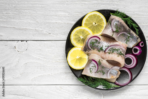 Canvas Print marinated herring fillet with pepper, herbs, onion and lemon on black plate on w