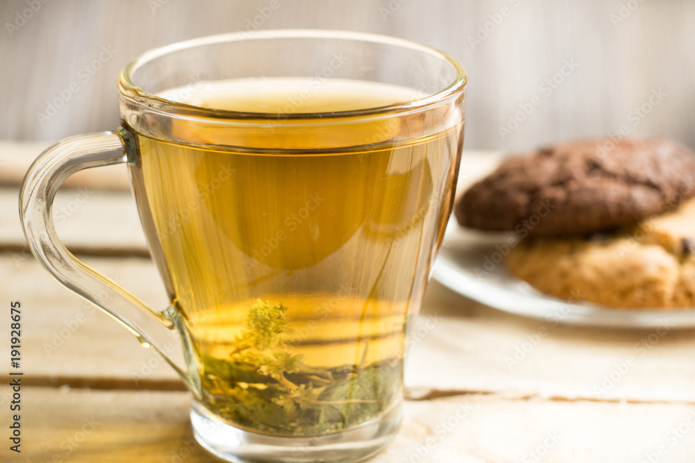 Transparent cup with herbal tea and an American chocolate chip cookie on a transparent plate on a wooden table Transparent cup with herbal tea and an American chocolate chip cookie on a transparent plate on a wooden table