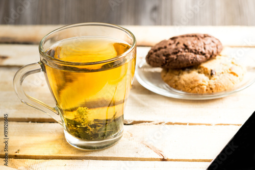 Transparent cup with herbal tea and an American chocolate chip cookie on a transparent plate on a wooden table