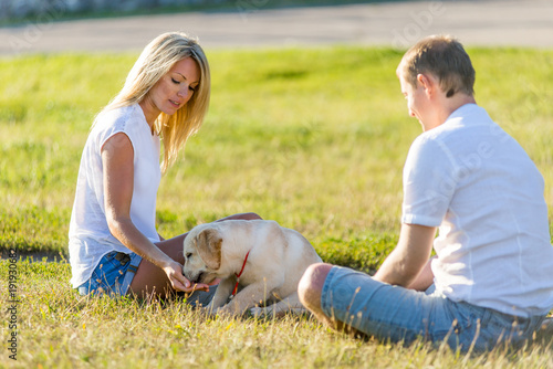 woman with a man playing with a labrador puppy in a park on the grass in the spring.