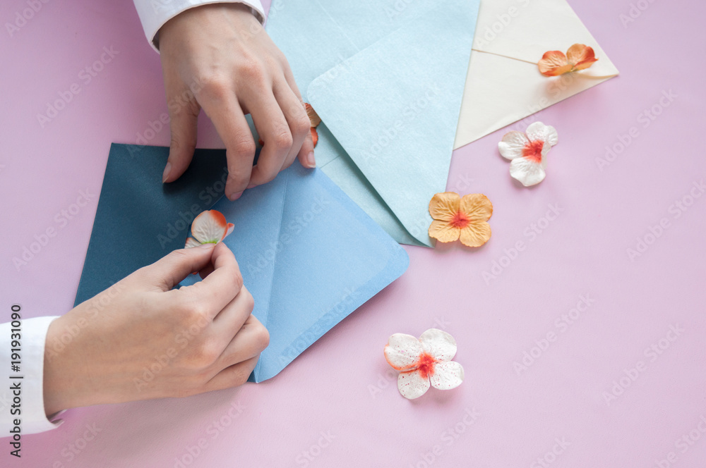 Female hands put the flower in a blue envelope on a pink background Female hands put the flower in a blue envelope on a pink background