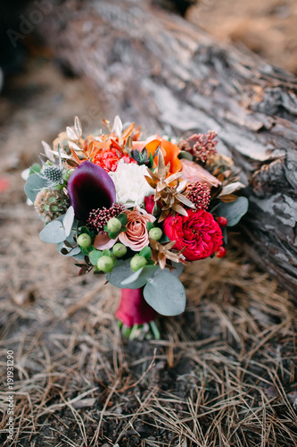 A rustic wedding bouquet with pink ribbons near the log. Artwork
