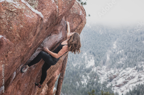 Fotografie, Obraz Female climber wearing black bouldering with snow and trees in the background