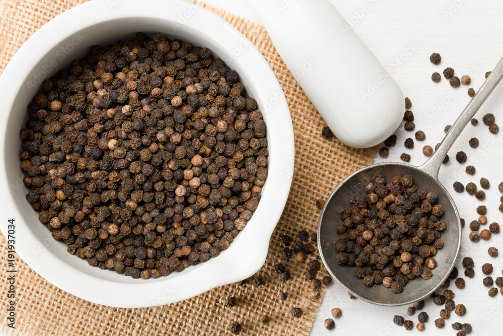 Raw, natural, unprocessed black pepper peppercorns in mortar and metal spoon Raw, natural, unprocessed black pepper peppercorns in mortar and metal spoon