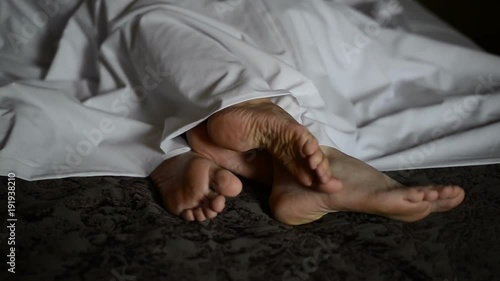 Female and male feet are lying upon each other under the tablecloth photo