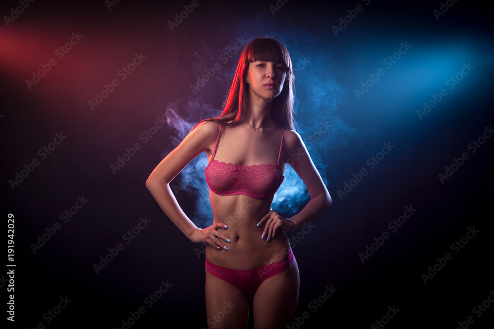 Young dark-haired woman in red lingerie posing against a background of red and red smoke from a wipe on a black isolated background