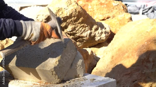 A stonecutter or stonemason is profiling the cut of a stone with a wide chisel. He is cutting the stone in a traditional way, manually. Closeup.