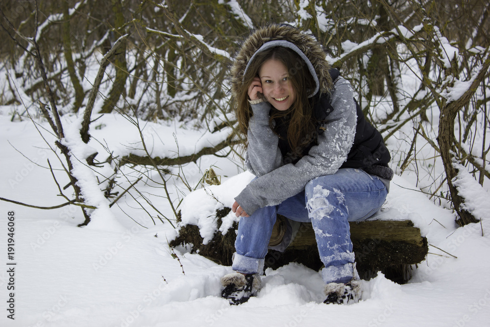 Pretty young woman sitting on the snow in the forest and talking on mobile phone. Nice smile. Cloudy winter day. Pretty young woman sitting on the snow in the forest and talking on mobile phone. Nice smile. Cloudy winter day.