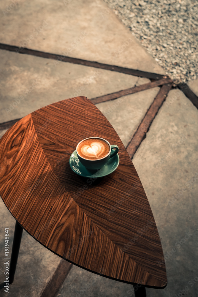 Turquoise mug of flat white coffee with heart shaped latte art in sunlight on wooden table at the hipster coffee shop.  Vintage color filter effect