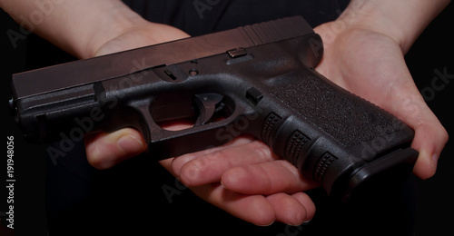 A close up of a girl's hands holding a black pistol on a black background