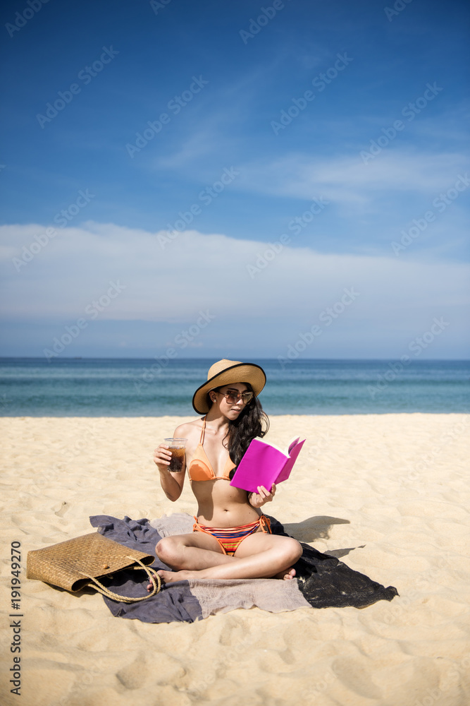 Happy woman traveler relaxing on a perfect beach. reading a book take soft drink in hand. background white sand and blue sea