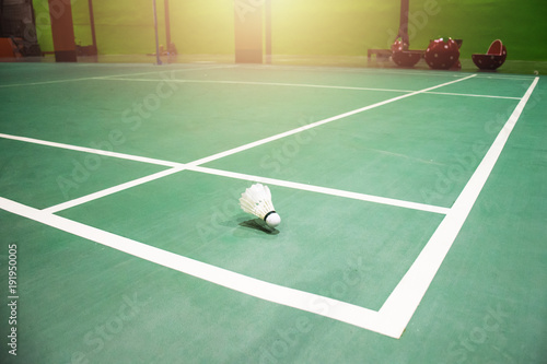 White badminton shuttlecock on a green floor with blurred players in badminton court