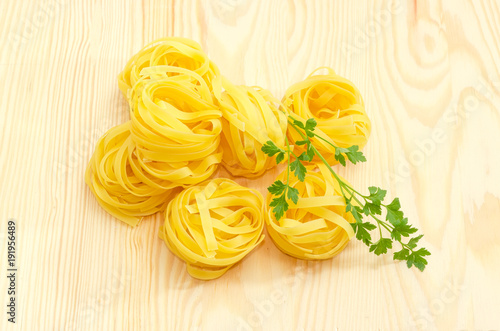Uncooked noodle nests with parsley twig on a wooden surface
