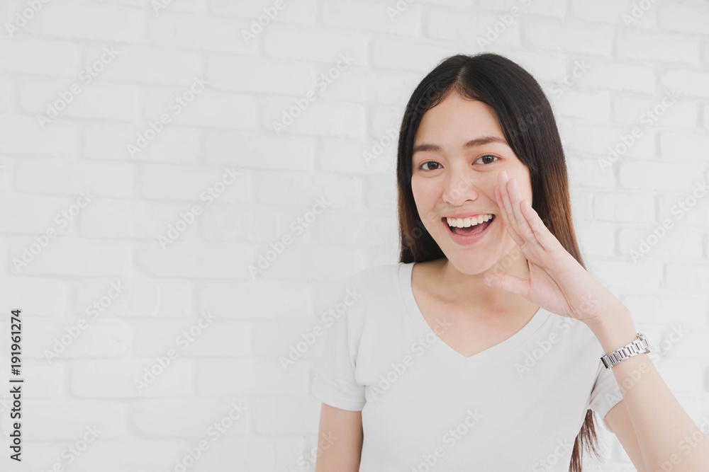 Happy smiling beautiful Asian woman gesturing with hand to telling in a white brick wall background. Happy smiling beautiful Asian woman gesturing with hand to telling in a white brick wall background.