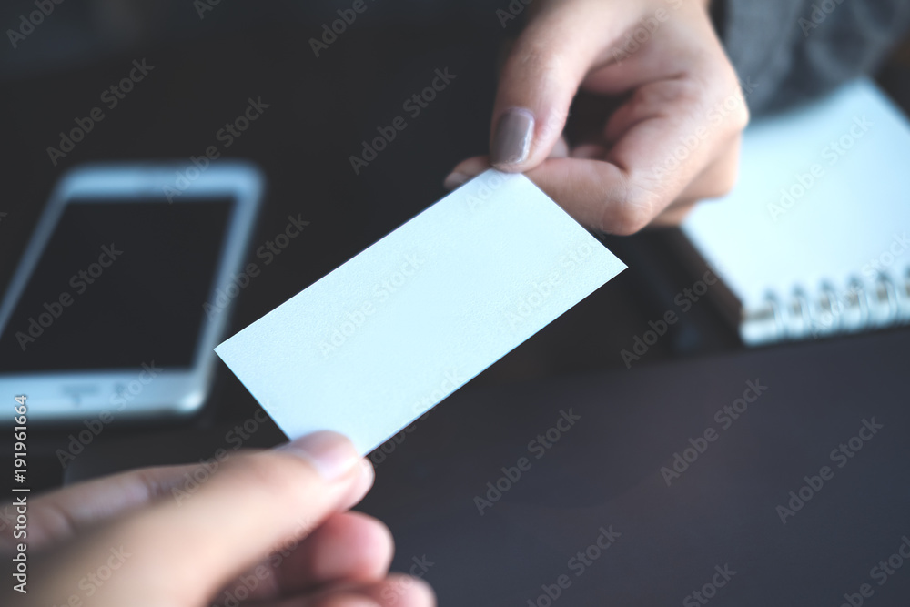 Businessman giving  business card to businesswoman with mobile phone and notebook on table in office