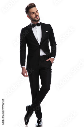 man in tuxedo standing with hand in pocket looks away