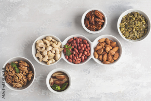 A variety of nuts and seeds in a white bowls, top view, copy space, food background. Healthy vegetarian food concept.