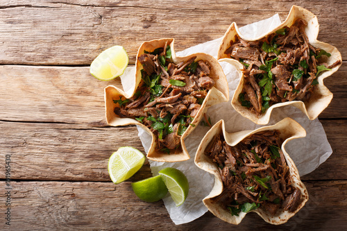 Pulled beef with lime and greens in a corn tortillas close-up on a table. horizontal top view
