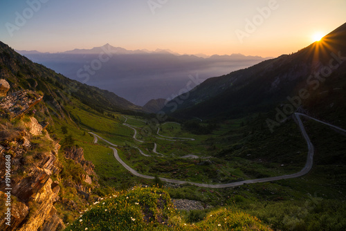 Dirt mountain road leading to high mountain pass in Italy (Colle delle Finestre). Expasive view at sunset, colorful dramatic sky, adventures in summer time, Italian Alps. photo