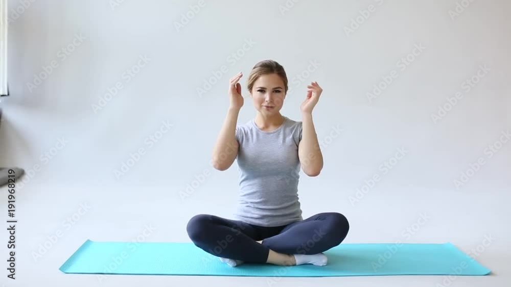 Beautiful young woman in sportswear practicing yoga while sitting in lotus position on gray background. Namaste. Beautiful young woman in sportswear practicing yoga while sitting in lotus position on gray background. Namaste.