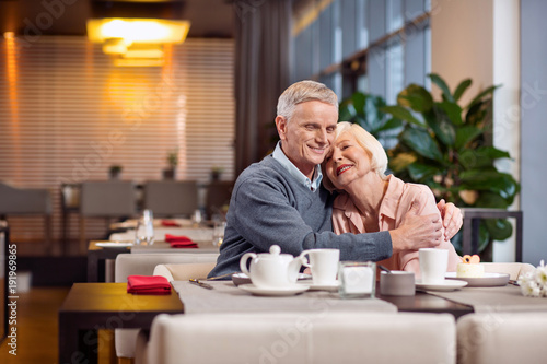 Partner support. Charming loving mature couple grinning while embracing and visiting restaurant