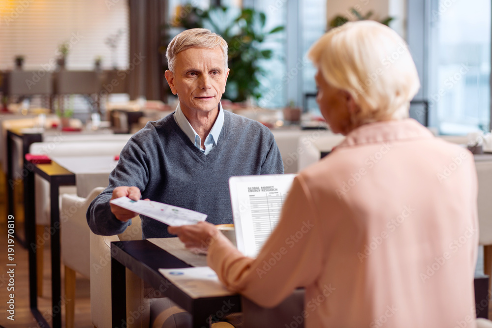 Evaluate this. Handsome thoughtful mature colleague compiling business plan while posing at restaurant and exchanging documents Evaluate this. Handsome thoughtful mature colleague compiling business plan while posing at restaurant and exchanging documents