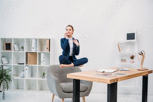 beautiful young businesswoman talking by smartphone while levitating at workplace