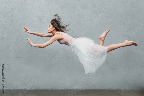 beautiful young woman in dress levitating and looking away on grey photo