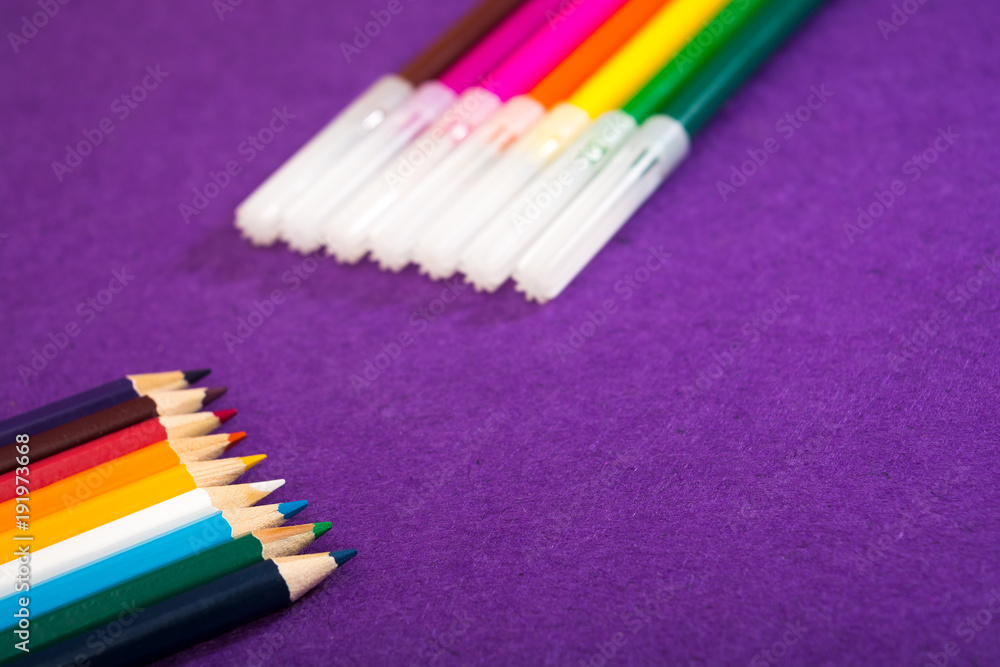 Fototapeta premium Seven multicolored felt pens and nine different colored pencils on a purple felt background with space for text. Back to school. Art lessons.