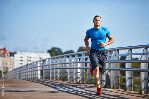 Fototapet Handsome athletic man out jogging in the city