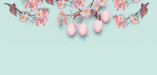 Easter banner with hanging pastel pink Easter eggs and spring blossom at light at blue turquoise background. Copy space