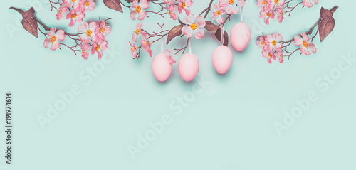 Easter banner with hanging pastel pink Easter eggs and spring blossom at light at blue turquoise background. Copy space