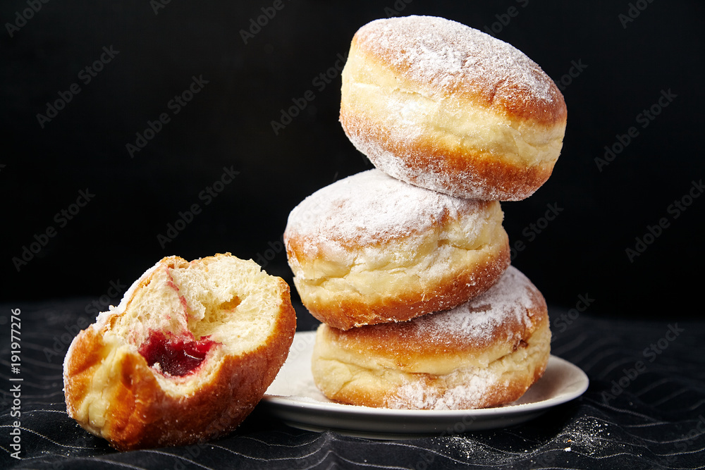 A stack of three sufganiyot donuts with jelly on black background A stack of three sufganiyot donuts with jelly on black background