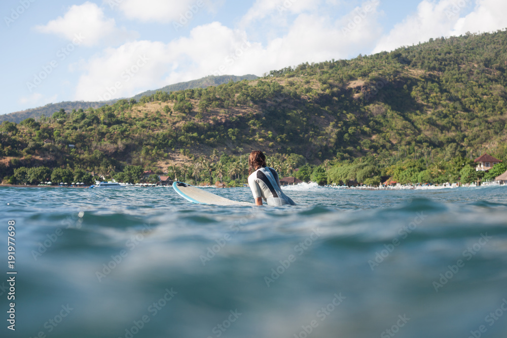 sportswoman swimming on surf board in ocean, coastline on background