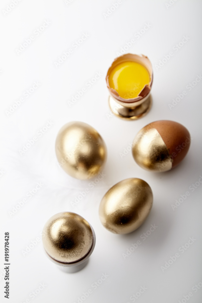 Eggs painted golden with yolk in egg stand on white background. Easter concept, copy space