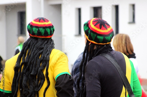 Bild auf Leinwand carnival, two men with jamaica caps and rasta wig, rear view