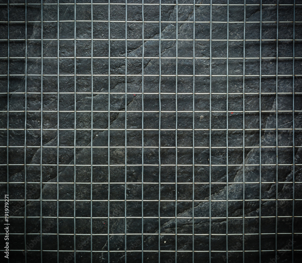 Metal mesh on black stone wall background in the dark Metal mesh on black stone wall background in the dark